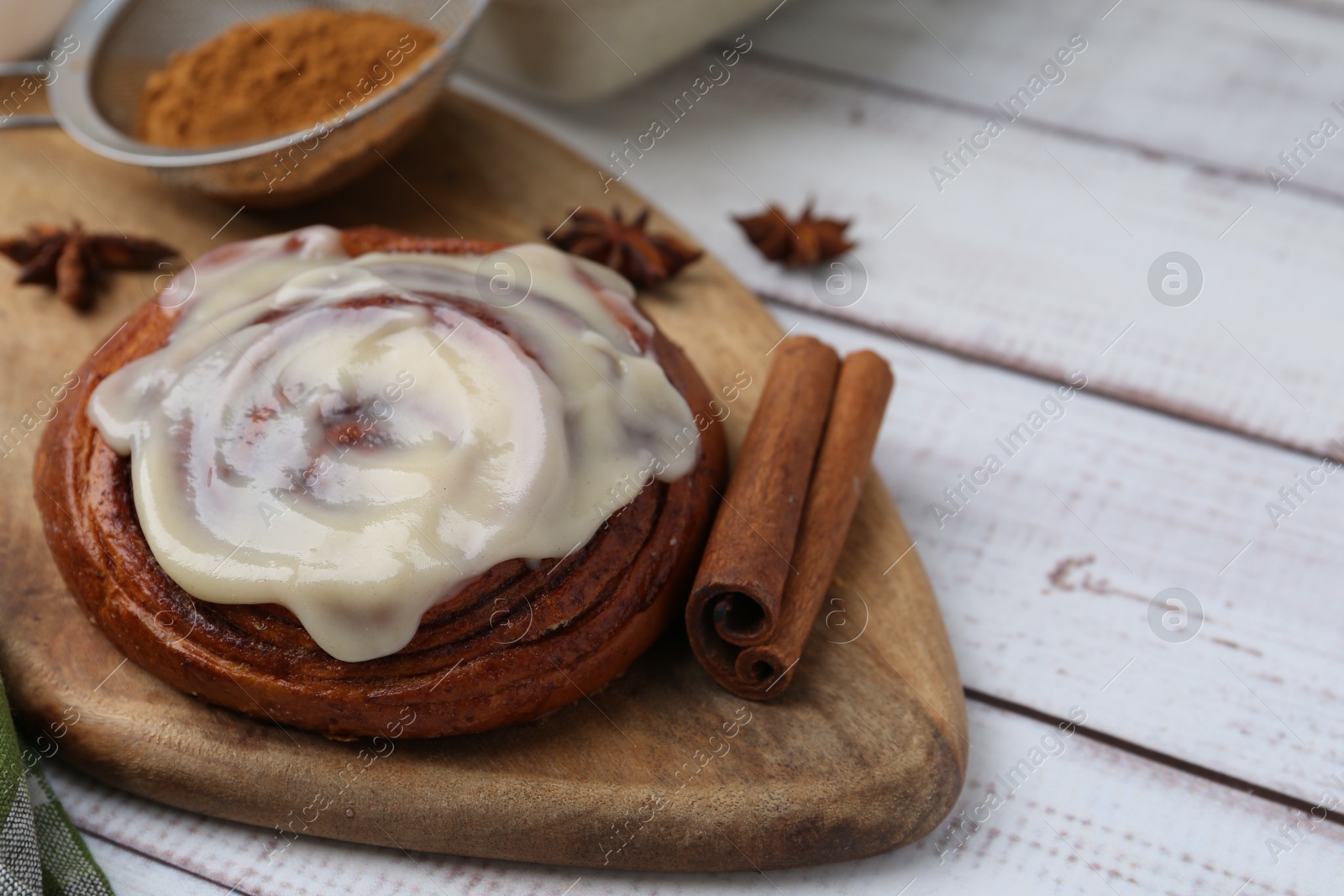 Photo of Tasty cinnamon roll with cream and spices on white wooden table, closeup. Space for text