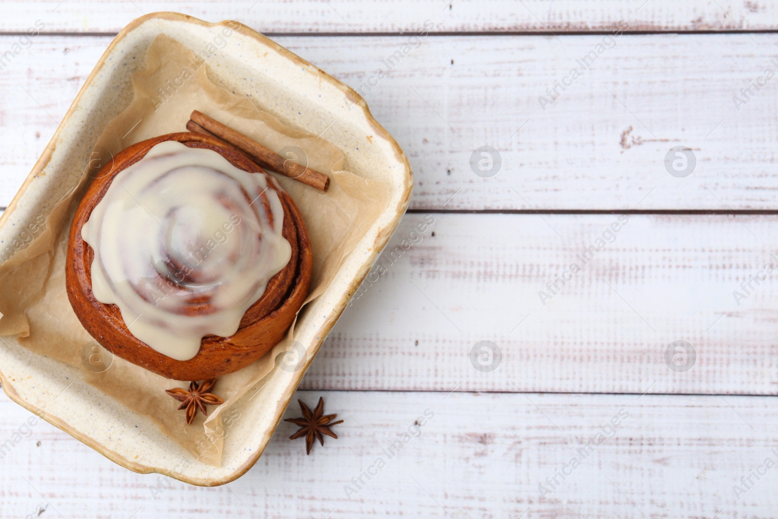 Photo of Tasty cinnamon roll with cream and spices in baking dish on white wooden table, top view. Space for text