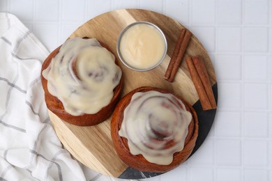 Photo of Tasty cinnamon rolls with cream and spices on white tiled table, top view