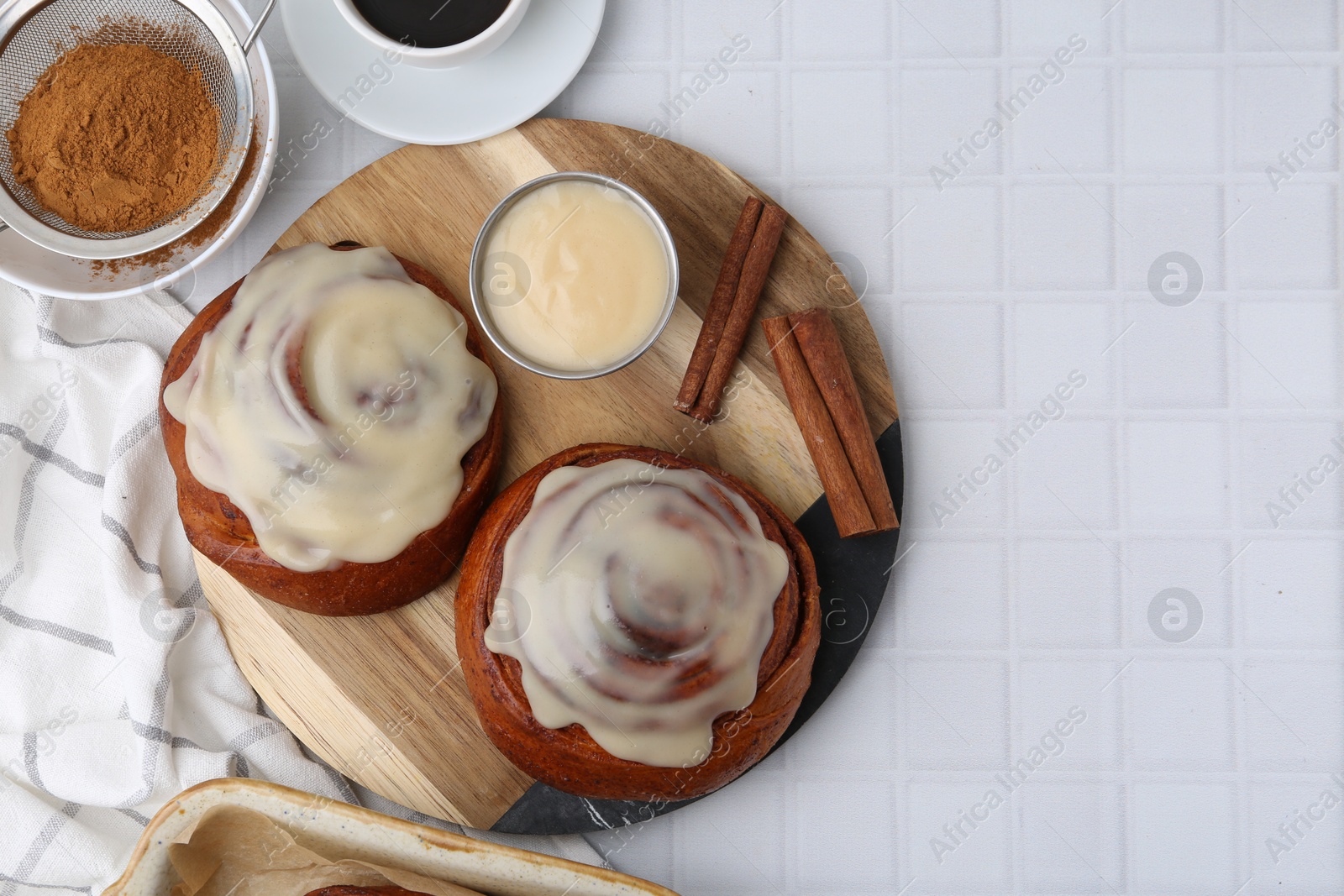 Photo of Tasty cinnamon rolls with cream, spices and coffee on white tiled table, flat lay. Space for text