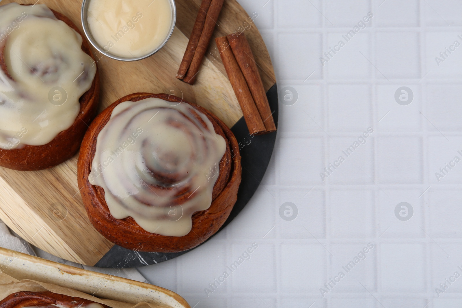 Photo of Tasty cinnamon rolls with cream and spices on white tiled table, flat lay. Space for text