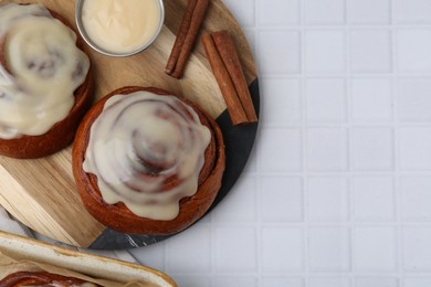 Photo of Tasty cinnamon rolls with cream and spices on white tiled table, flat lay. Space for text