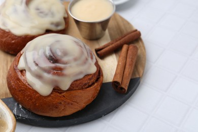 Photo of Tasty cinnamon rolls with cream and spices on white tiled table, closeup. Space for text