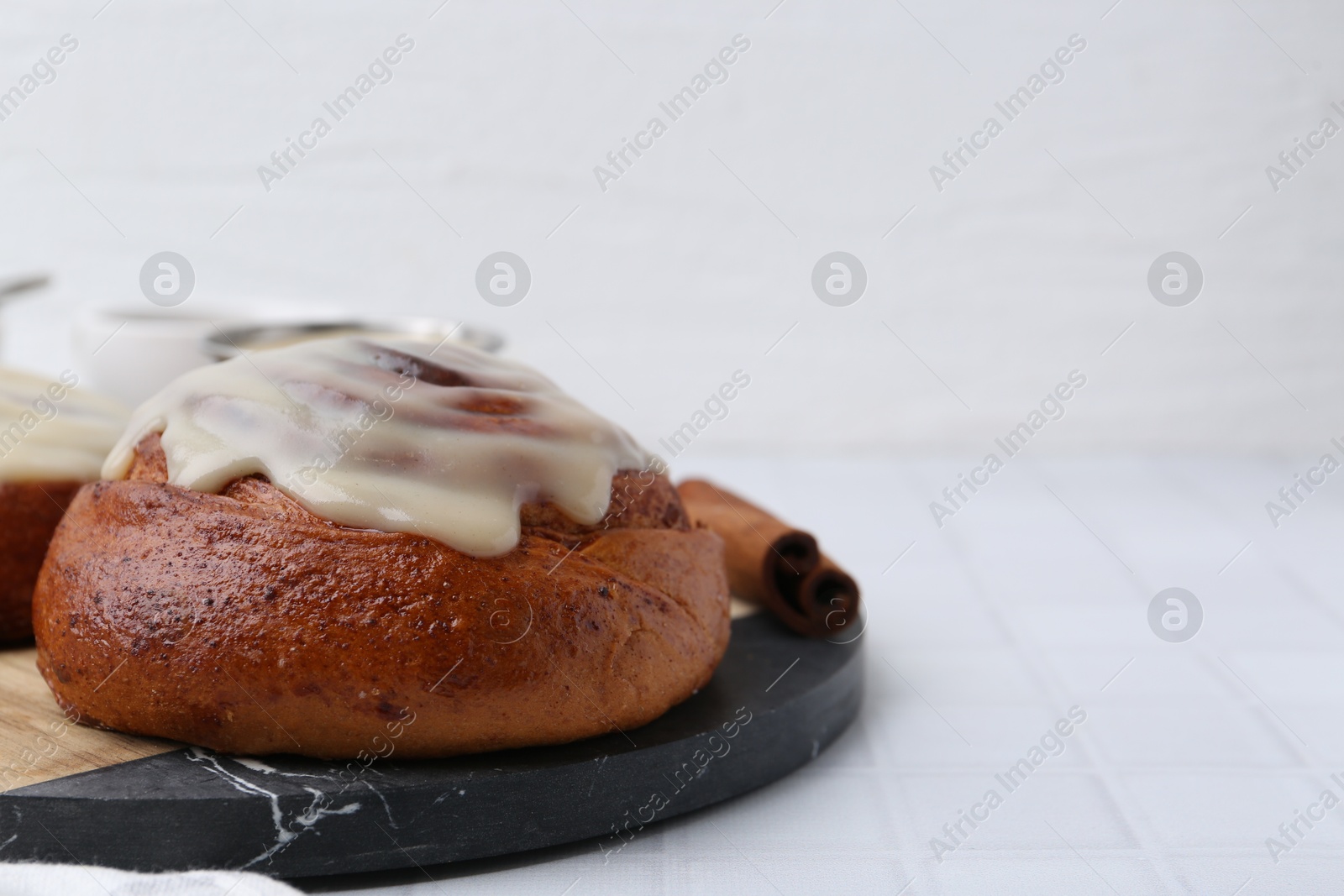 Photo of Tasty cinnamon roll with cream on white tiled table, closeup. Space for text