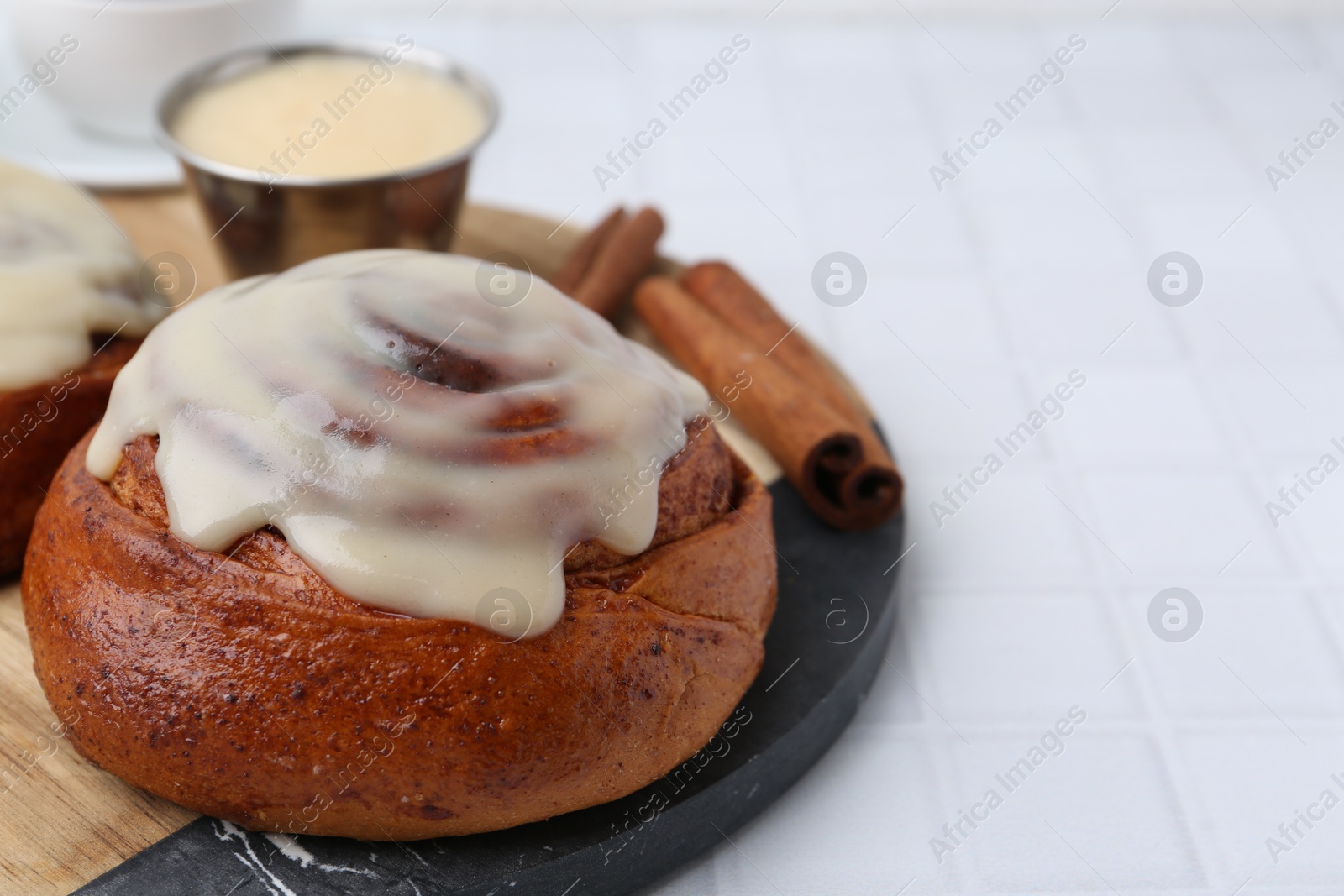 Photo of Tasty cinnamon roll with cream and spices on white tiled table, closeup. Space for text