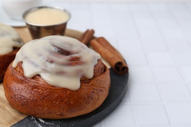 Photo of Tasty cinnamon roll with cream and spices on white tiled table, closeup. Space for text