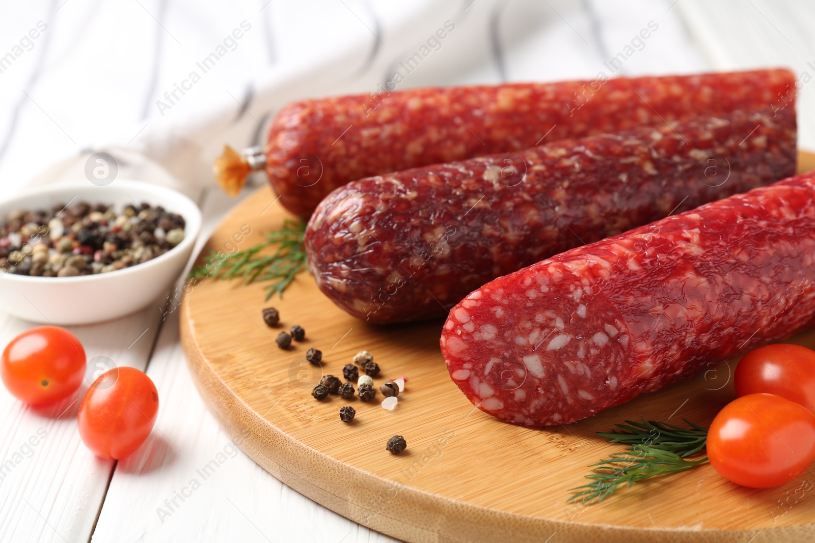 Photo of Different smoked sausages, cherry tomatoes and spices on white wooden table, closeup