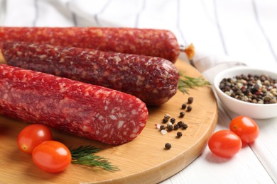 Photo of Different smoked sausages, cherry tomatoes and spices on white wooden table, closeup