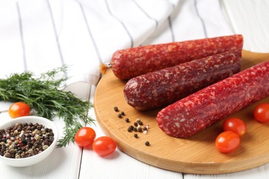 Photo of Different smoked sausages, cherry tomatoes and spices on white wooden table, closeup