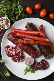 Photo of Different smoked sausages, cherry tomatoes and spices on dark wooden table, flat lay