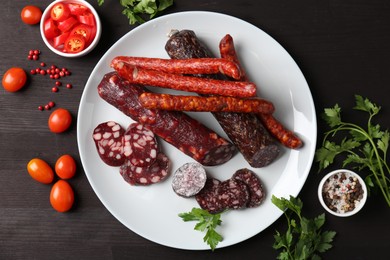 Photo of Different smoked sausages, cherry tomatoes and spices on dark wooden table, flat lay