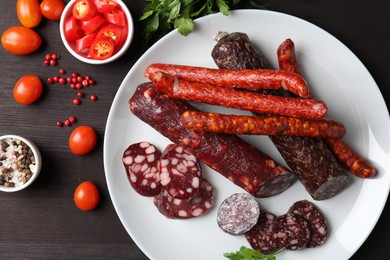 Photo of Different smoked sausages, cherry tomatoes and spices on dark wooden table, flat lay