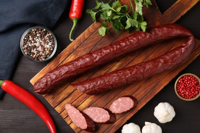 Photo of Delicious thin smoked sausage and spices on dark wooden table, flat lay