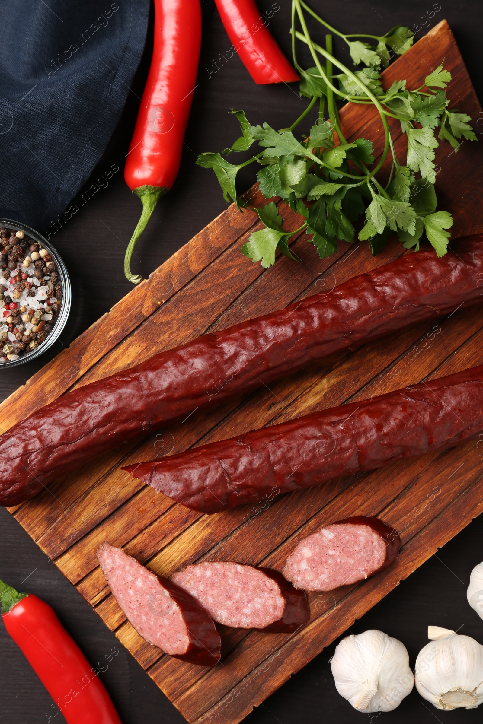 Photo of Delicious thin smoked sausage and spices on dark wooden table, flat lay