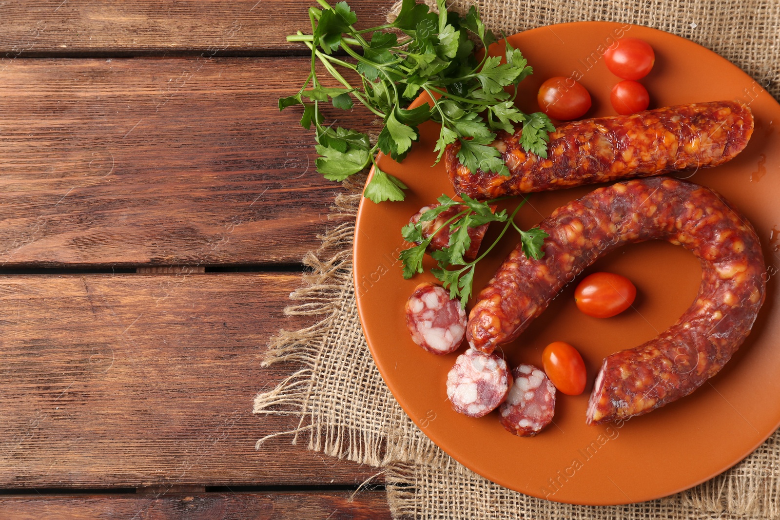 Photo of Different smoked sausages, cherry tomatoes and parsley on wooden table, top view. Space for text