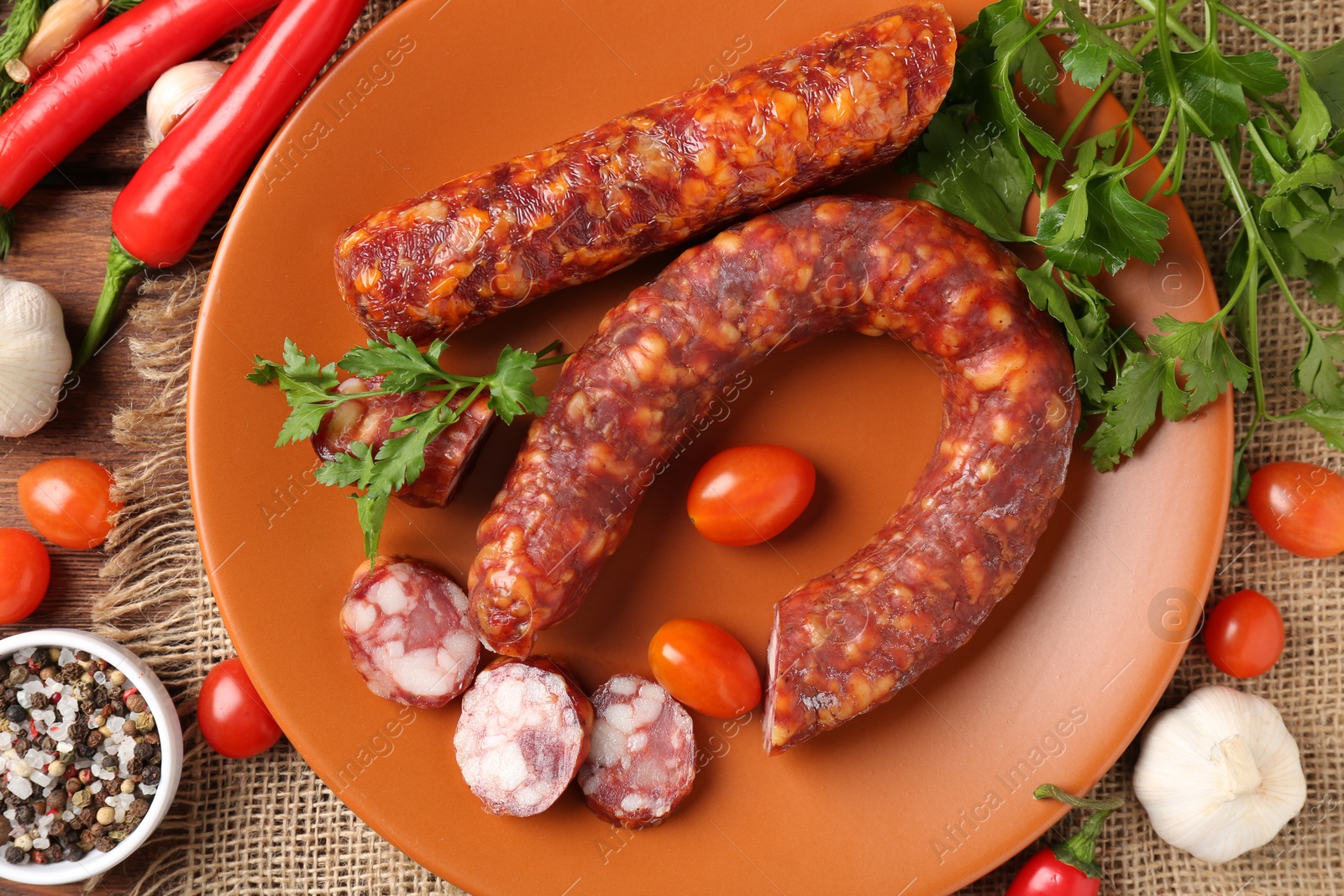 Photo of Different smoked sausages, cherry tomatoes and spices on table, flat lay