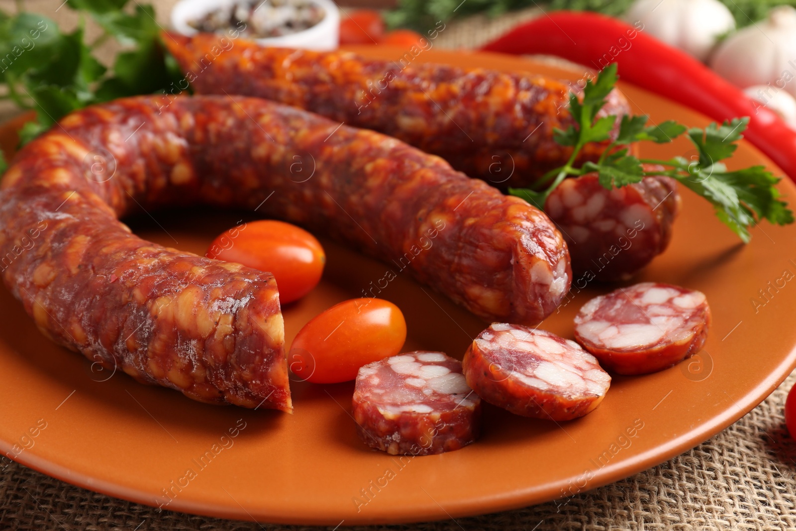 Photo of Different smoked sausages, cherry tomatoes and spices on table, closeup