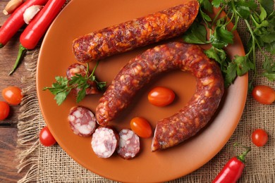 Photo of Different smoked sausages, cherry tomatoes and spices on wooden table, flat lay