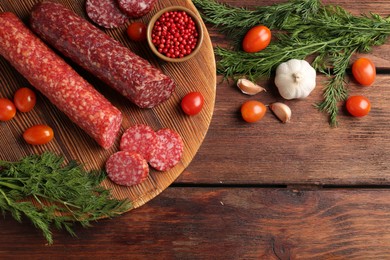 Photo of Different smoked sausages, cherry tomatoes and spices on wooden table, flat lay. Space for text