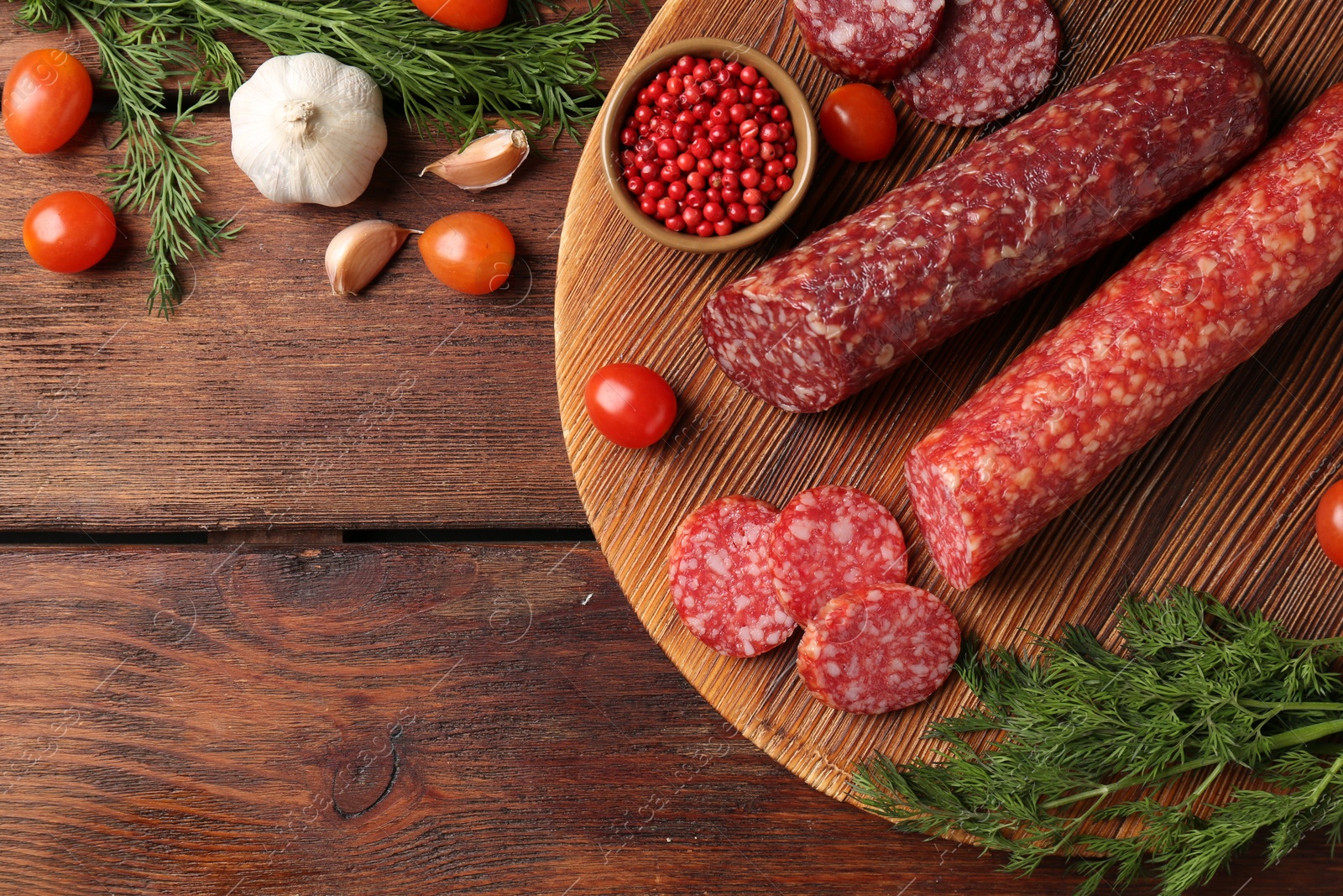 Photo of Different smoked sausages, cherry tomatoes and spices on wooden table, flat lay. Space for text