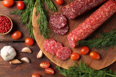 Photo of Different smoked sausages, cherry tomatoes and spices on wooden table, flat lay