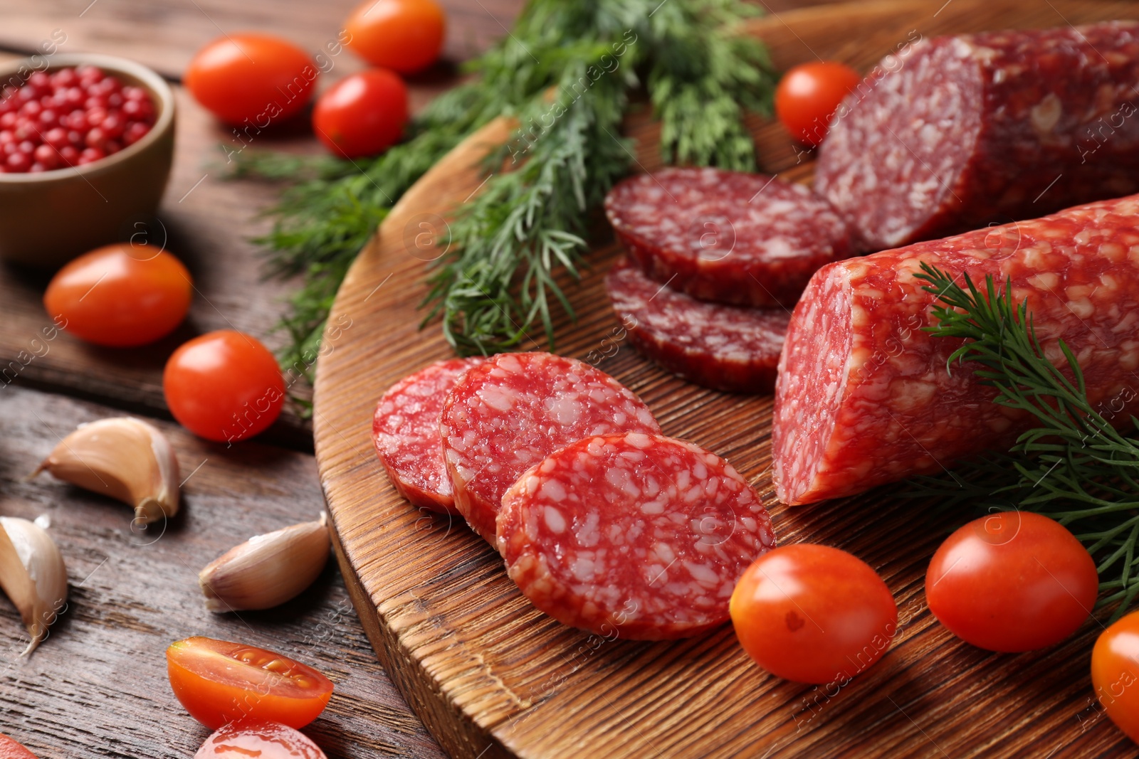 Photo of Different smoked sausages, cherry tomatoes and spices on wooden table, closeup