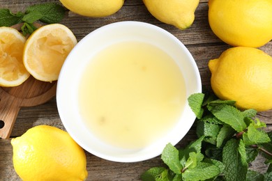 Photo of Fresh lemon juice in bowl and fruits on wooden table, flat lay