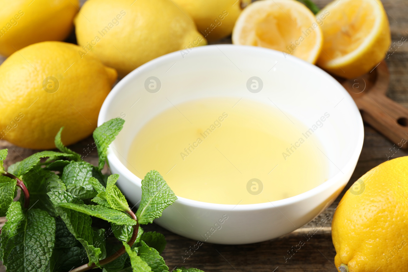 Photo of Fresh lemon juice in bowl and fruits on wooden table, closeup