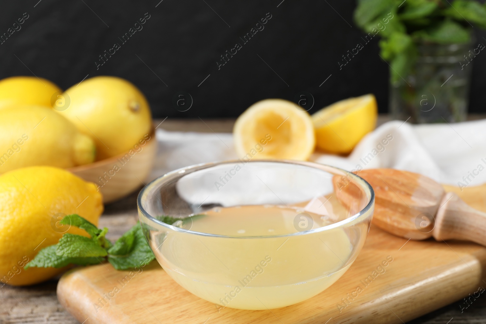 Photo of Fresh lemon juice in bowl, squeezer and fruits on wooden table, closeup