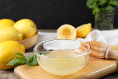 Photo of Fresh lemon juice in bowl, squeezer and fruits on wooden table, closeup