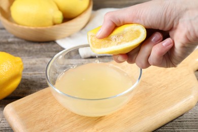 Photo of Woman squeezing lemon juice into bowl at wooden table, closeup