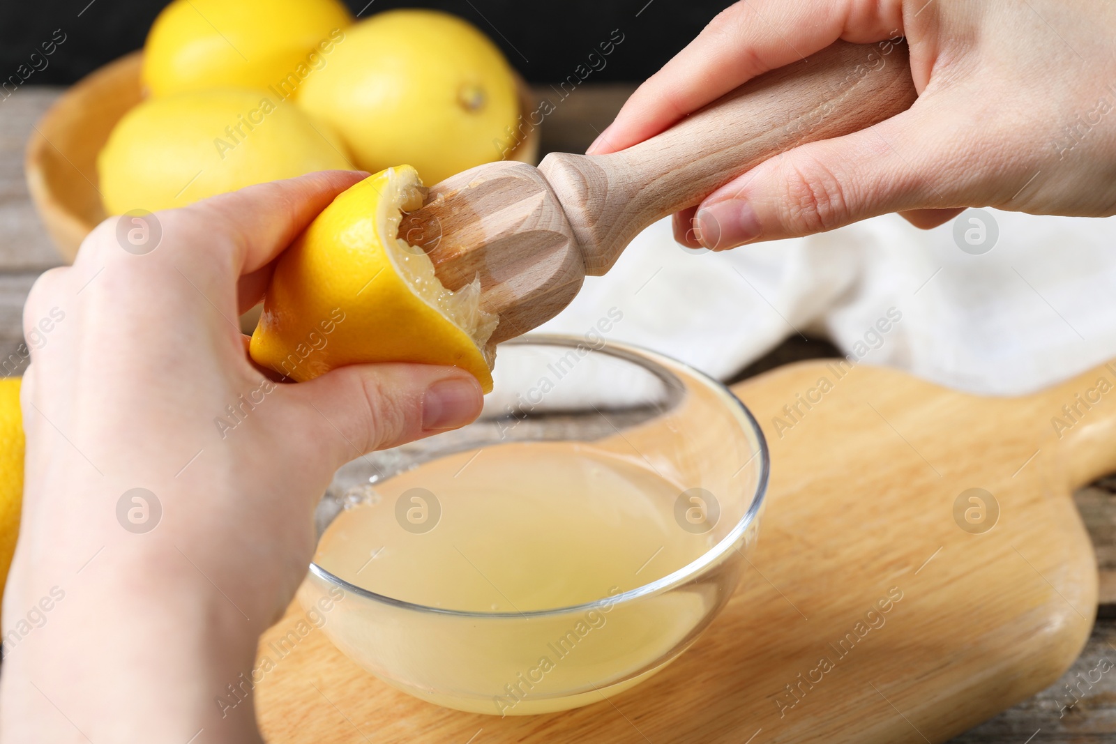 Photo of Woman juicing lemon into bowl at wooden table, closeup