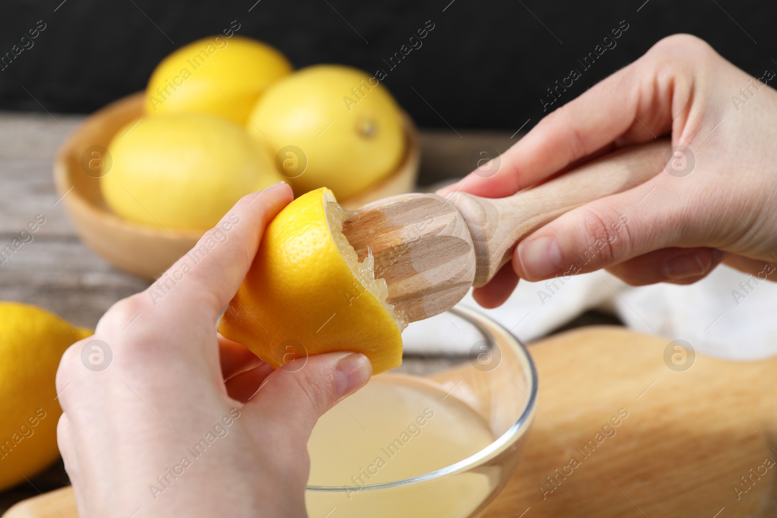 Photo of Woman juicing lemon into bowl at wooden table, closeup