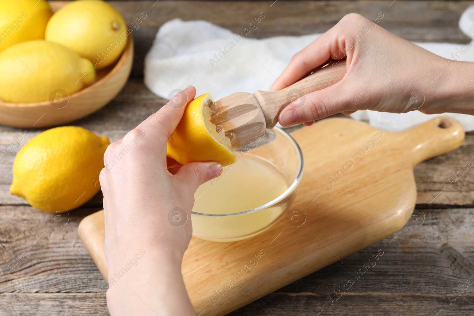 Photo of Woman juicing lemon into bowl at wooden table, closeup