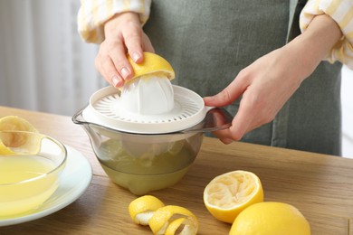 Photo of Woman with lemon using juicer at wooden table, closeup