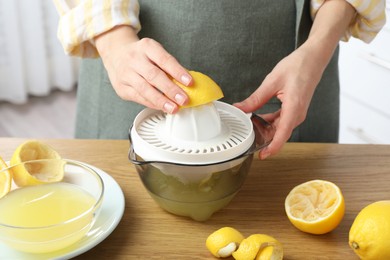 Photo of Woman with lemon using juicer at wooden table, closeup