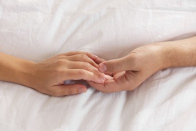 Photo of Lovely couple holding hands in bed, top view