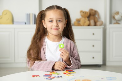 Photo of Little girl learning alphabet with magnetic letters at white table indoors