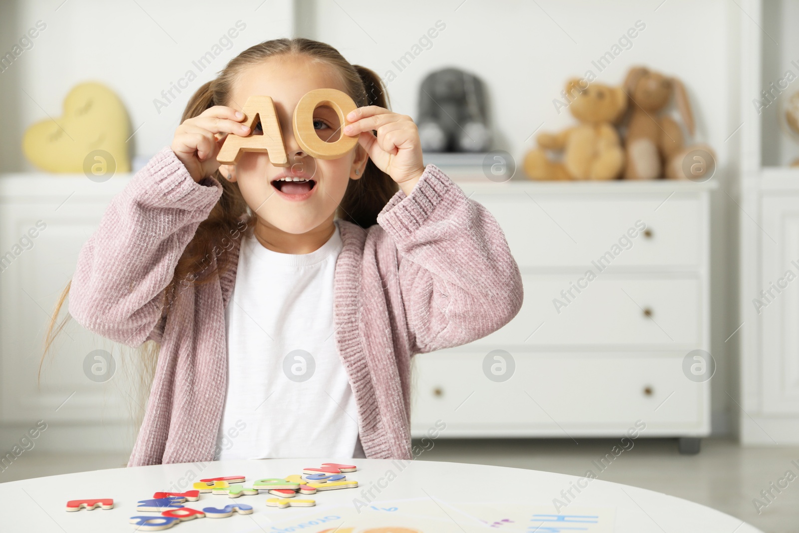 Photo of Little girl learning alphabet with different letters at white table indoors, space for text