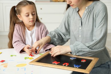 Photo of Speech therapist teaching little girl alphabet with magnetic letters at white table indoors, closeup