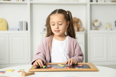 Photo of Little girl learning alphabet with magnetic letters at white table indoors