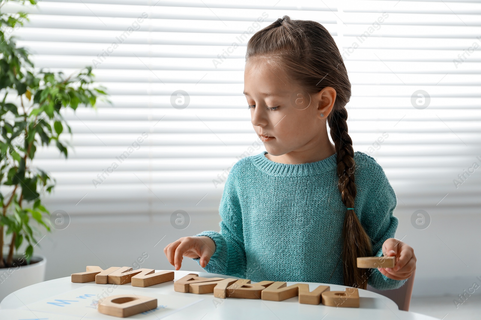 Photo of Little girl learning alphabet with wooden letters at white table indoors