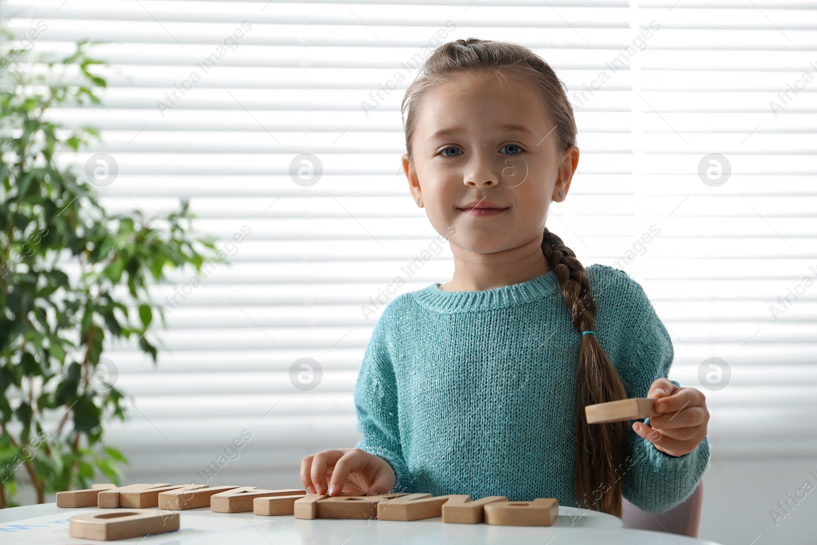 Photo of Little girl learning alphabet with wooden letters at white table indoors