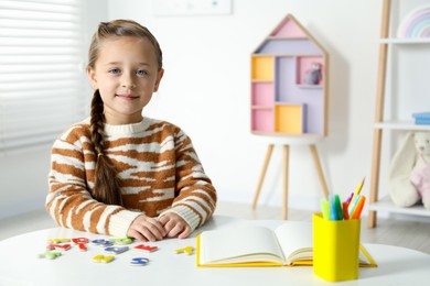 Photo of Little girl learning alphabet with magnetic letters at white table indoors