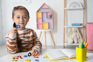 Photo of Little girl learning alphabet with magnetic letters at white table indoors