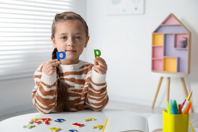 Photo of Little girl learning alphabet with magnetic letters at white table indoors