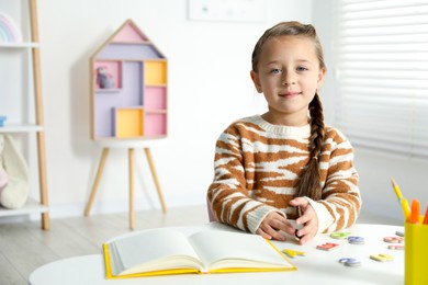 Photo of Little girl learning alphabet with magnetic letters at white table indoors