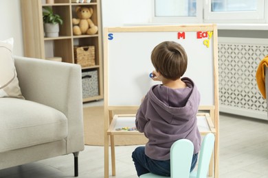 Photo of Little boy learning alphabet with magnetic letters indoors, back view