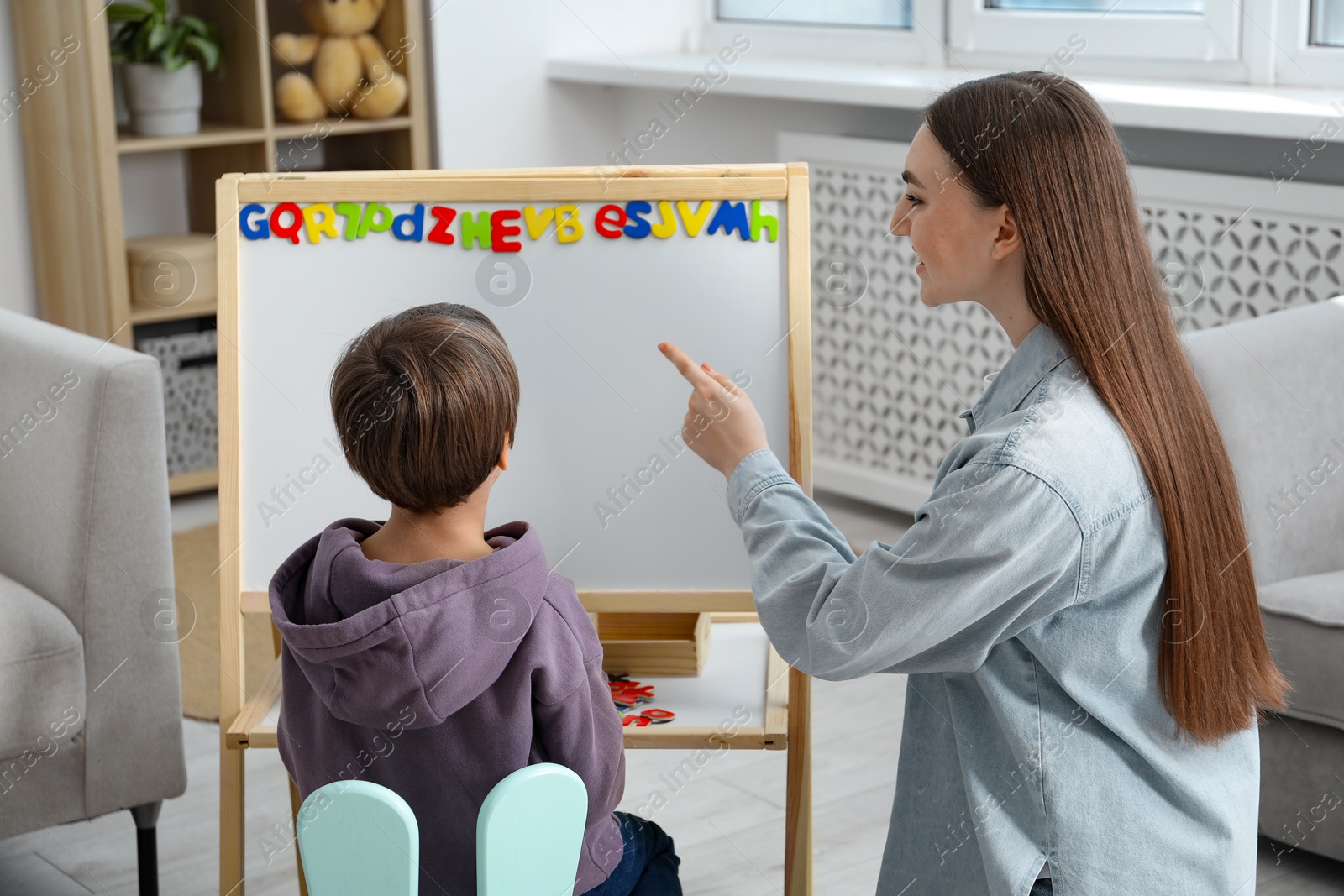 Photo of Speech therapist teaching little boy alphabet with magnetic letters indoors