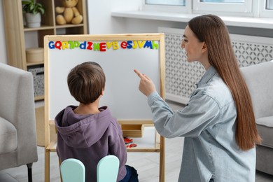 Photo of Speech therapist teaching little boy alphabet with magnetic letters indoors